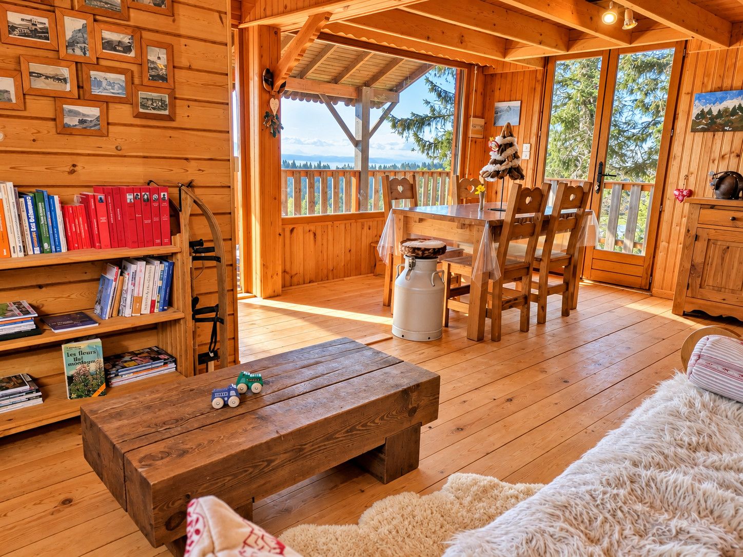 A wooden cabin interior with a dining area, bookshelves, and a view of the outdoors.