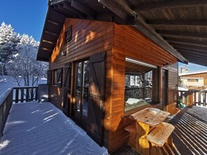 Eine Holzhütte mit überdachter Veranda, einer Bank und Blick auf verschneite Bäume.