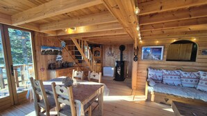 L’intérieur d’un chalet en bois comprend un coin repas, un canapé, une cheminée et un escalier menant à une mezzanine.