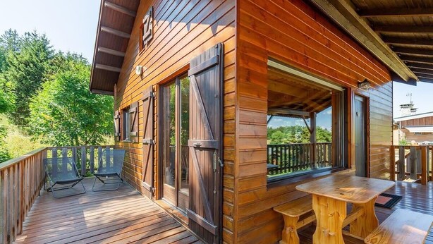 Une cabane en bois dotée d’une terrasse, de deux chaises et d’une table en bois.
