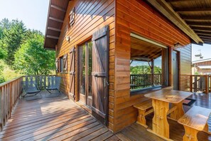 Une cabane en bois dotée d’une terrasse, de deux chaises et d’une table en bois.