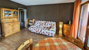 A cozy room with a wooden cabinet, a patterned sofa, a plaid tablecloth, and a lamp.