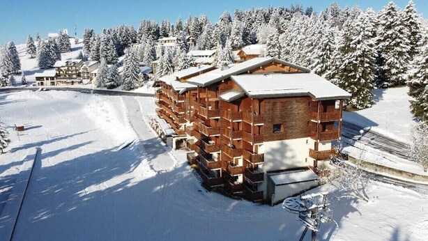 A wooden lodge with multiple balconies, surrounded by snow-covered trees and a ski slope.