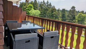 A balcony with a table and chairs, overlooking a forested area.
