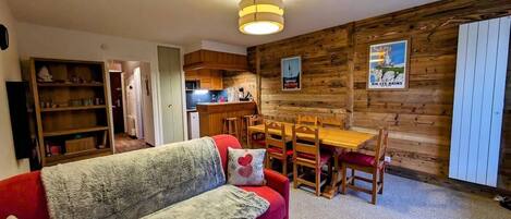 Een gezellige woonkamer met een rode bank, een houten eettafel en een keuken op de achtergrond.