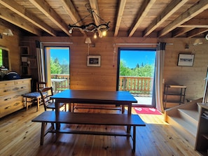 Un intérieur en bois comprenant une table à manger, des chaises, une commode et une vue sur l’extérieur.