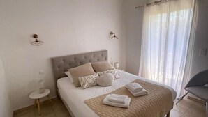 A neatly arranged bedroom with a bed, bedside tables, and a chair. - Mini Villa sur Santa Giulia (Porto-Vecchio)
