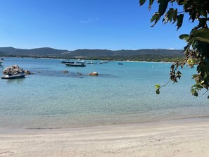 Uma praia com águas claras, barcos e montanhas ao longe.