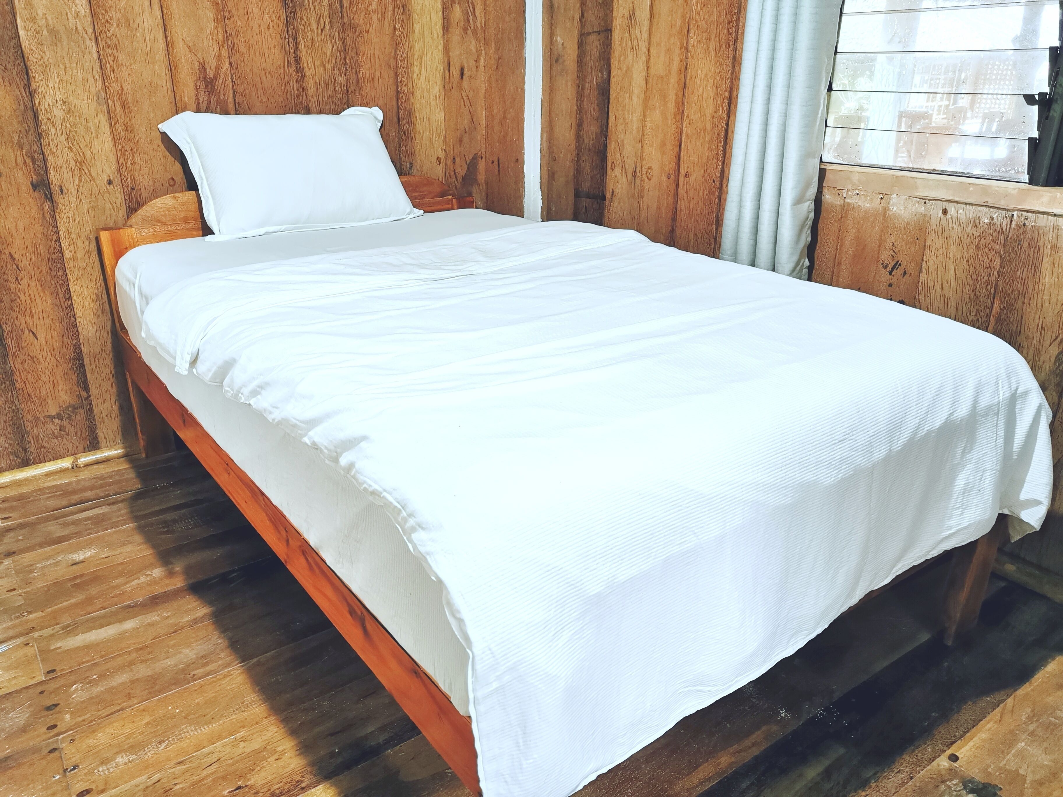 A single bed with a white mattress and pillow in a room with wooden walls and floors.