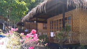 Una casa de madera tradicional con techo de paja, rodeada de abundante vegetación y plantas en flor.