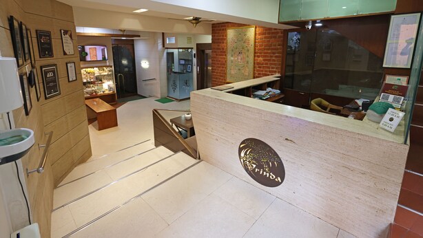 A reception area with a wooden counter, framed certificates on the wall, and a staircase leading to another floor. - Vrinda Hotel (Nathdwara)