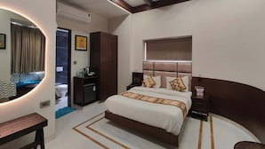A bedroom with a large bed, a bedside table, a nightstand, a mirror, and a wardrobe. - Vrinda Hotel (Nathdwara)