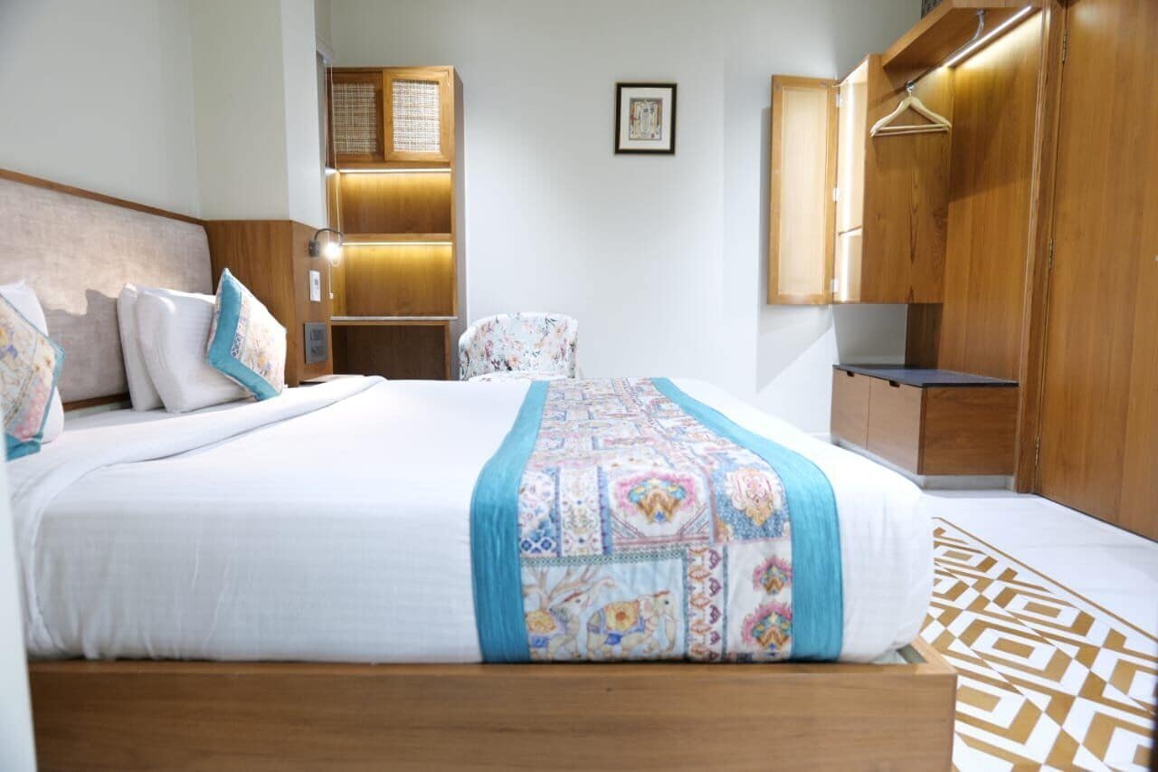 A hotel room with a large bed, wooden wardrobe, and a small seating area.