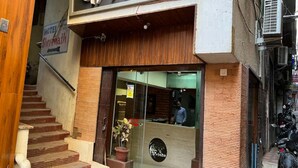 A hotel entrance with a staircase leading up, a reception desk, and a potted plant outside. - Vrinda Hotel (Nathdwara)