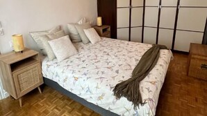 A bedroom with a bed, wooden nightstands, a woven lamp, and a hanging light fixture.
