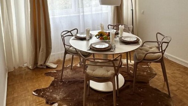 A dining area with a round table, chairs, a pendant light, and a fur rug on the floor.