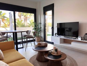 A modern living room with a sofa, a TV, a dining table with chairs, and a balcony with plants.