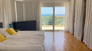 Un dormitorio con una cama grande, un aparador y vistas al océano a través de una puerta corrediza de vidrio.