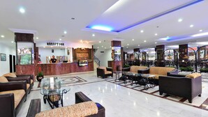 Un vestíbulo de hotel con mostrador de recepción, zonas de estar y una escalera.