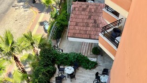 Una terraza al aire libre con varias mesas y sillas redondas, rodeada de abundante vegetación y un suelo de baldosas.