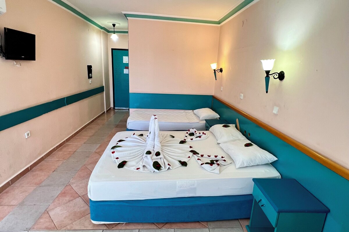A hotel room with a large bed, a television, and a wall-mounted light fixture.