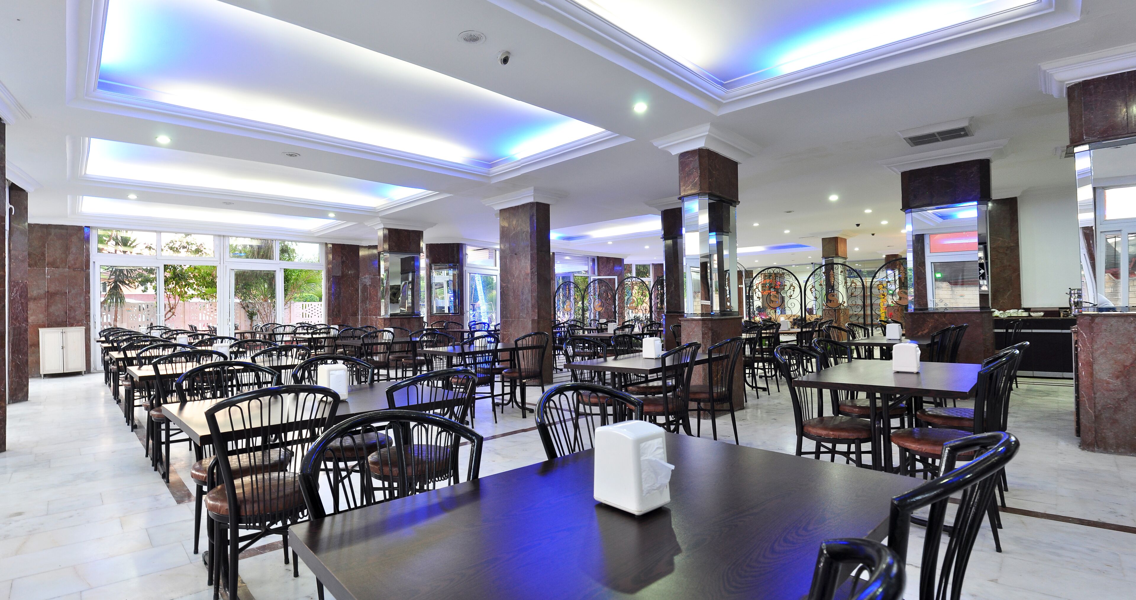 A spacious dining area with multiple tables and chairs, large windows, and a modern ceiling design.
