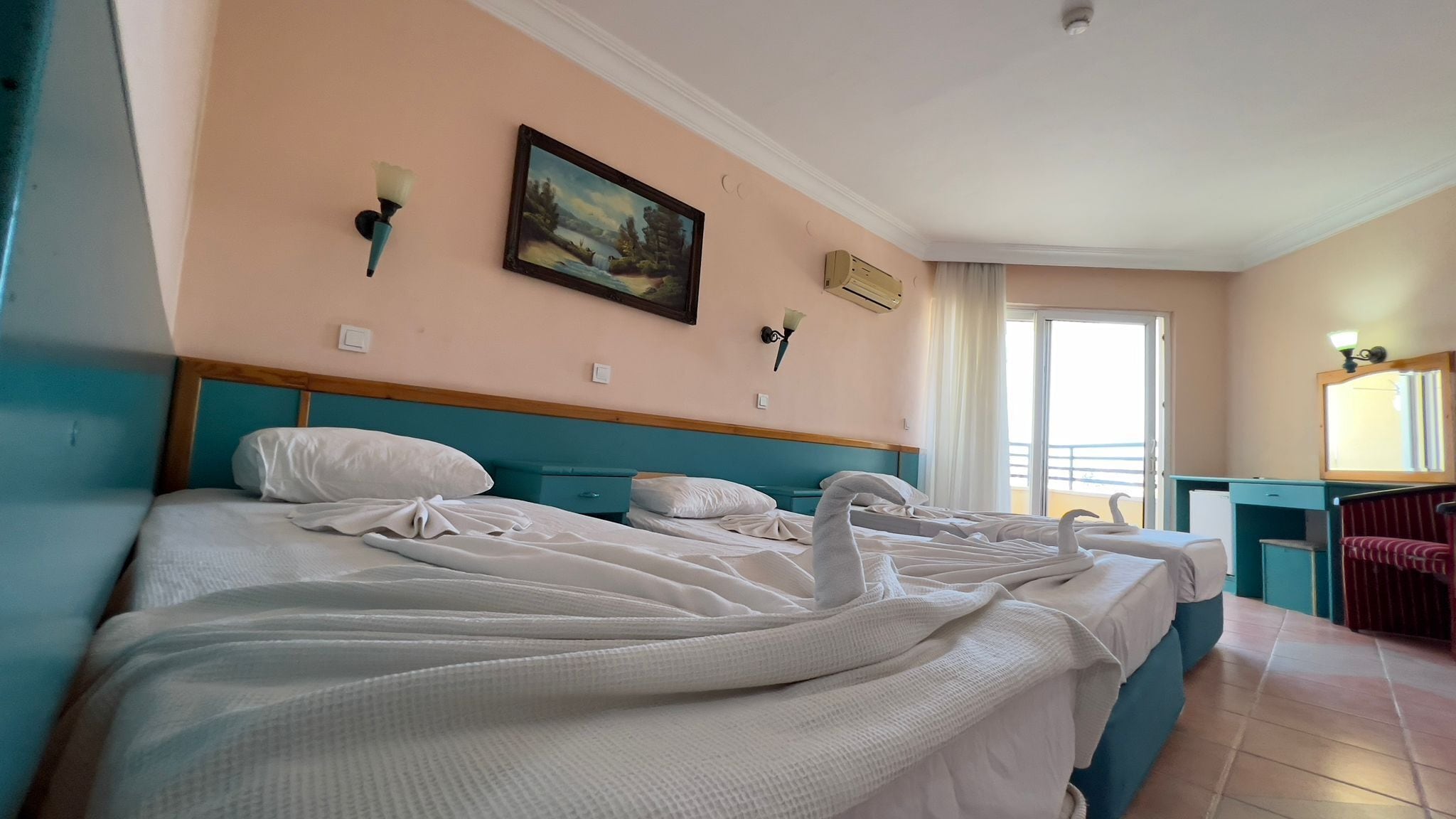 Ein Hotelzimmer mit zwei Betten, einem Bild an der Wand und Meerblick durch das Fenster.