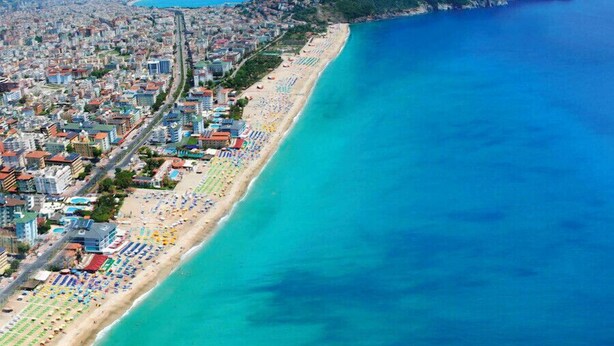 Vista aérea de una ciudad costera con una playa extensa bordeada de sombrillas de colores y edificios a lo largo de la orilla.