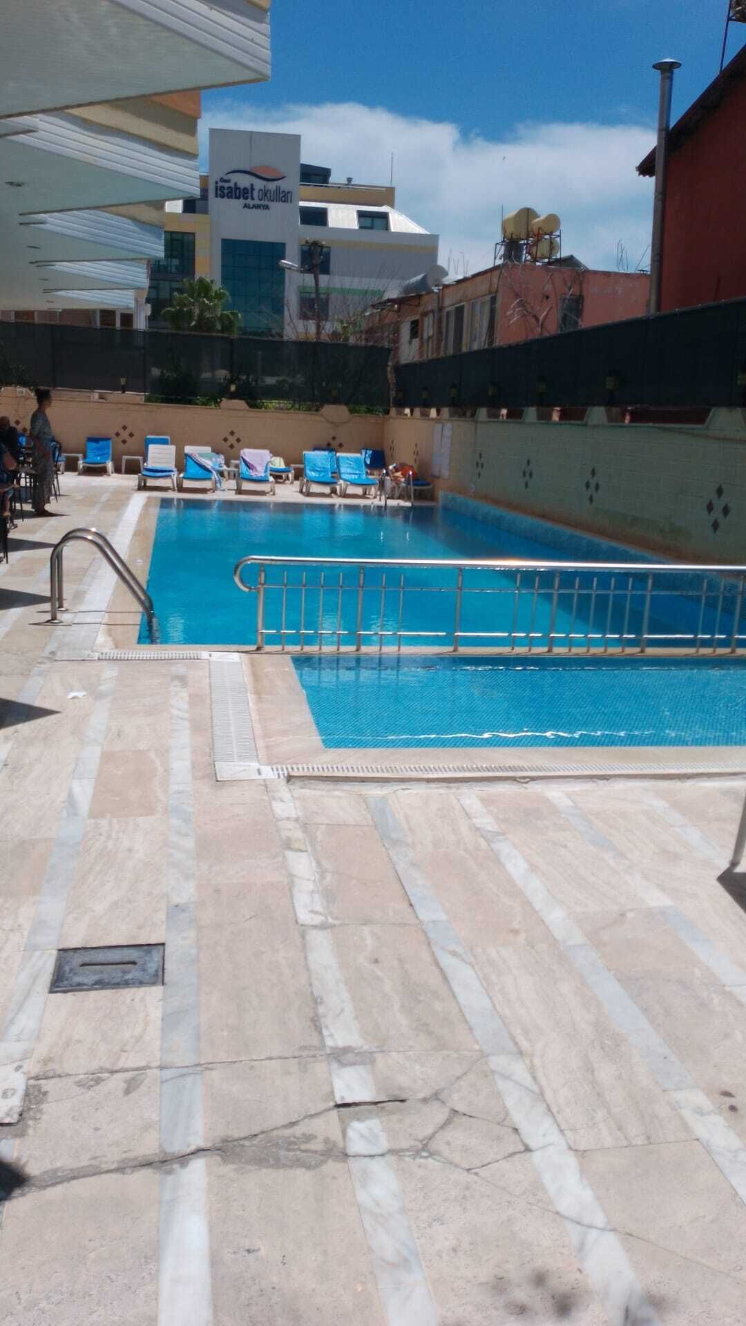 A swimming pool with a tiled deck, a metal safety railing, and lounge chairs.