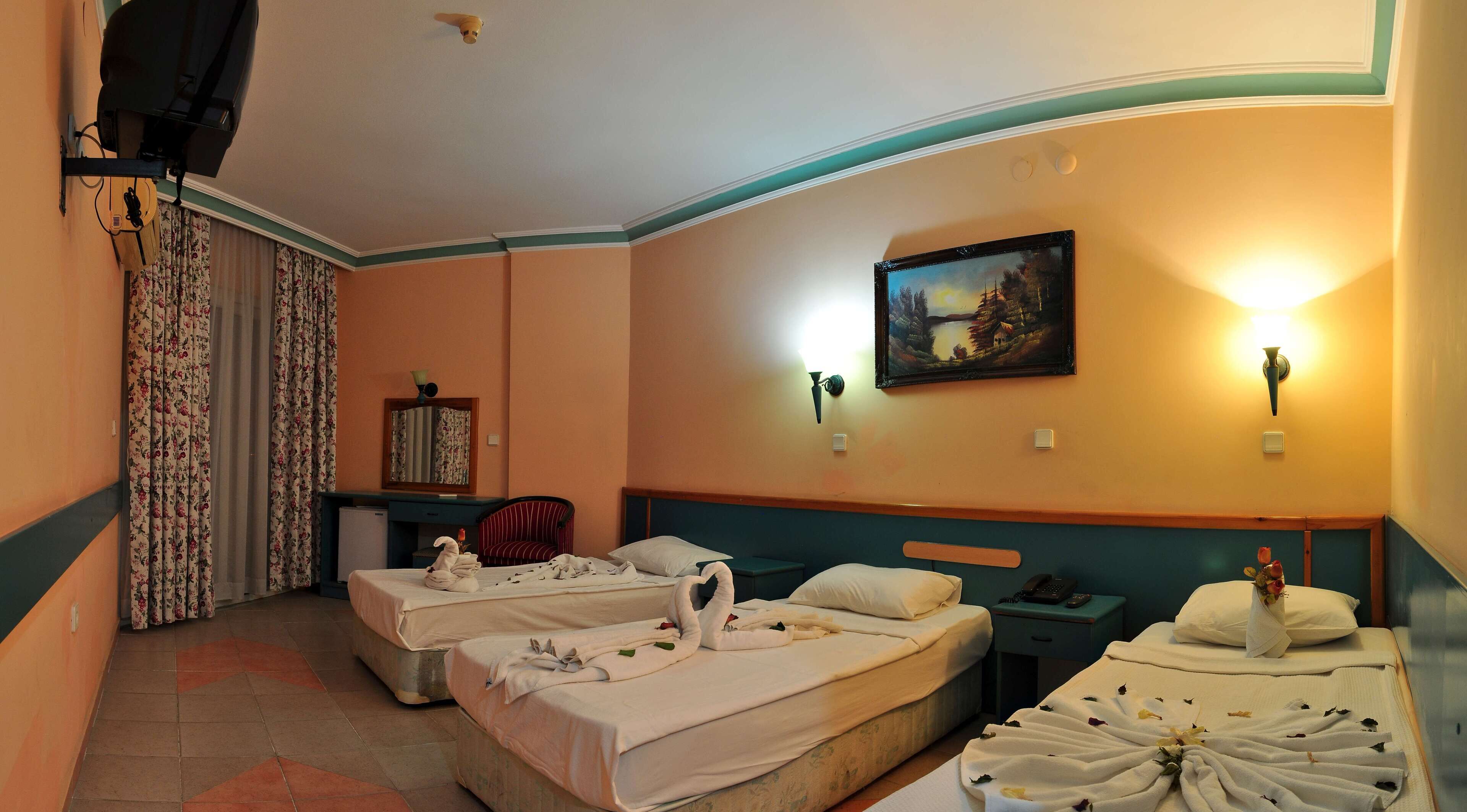 Hotellihuone, jossa on kaksi sänkyä, työpöytä, tuoli, taulu ja seinään kiinnitetty valaisin.