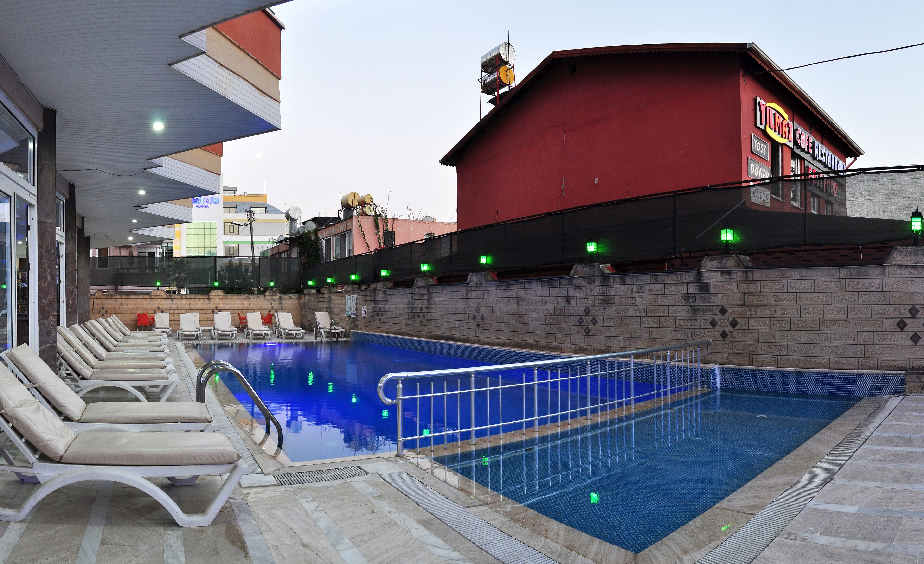 An indoor swimming pool with lounge chairs and a red building in the background.