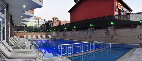 An indoor swimming pool with lounge chairs and a red building in the background.