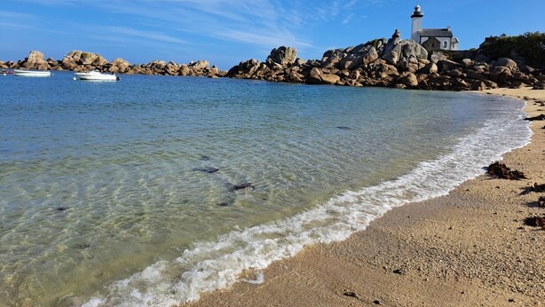 A coastal scene with clear water, a sandy beach, and a lighthouse on a rocky outcrop. - Maison Entièrement Rénovée ,à 600m de la mer Ideale Pour Passer de Bons Moments! (Plounéour-Brignogan-plages)