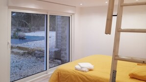 A bedroom with a wooden slatted ceiling, a bed with a yellow bedspread, a wooden ladder, and a large sliding glass door leading to an outdoor area. - Maison Entièrement Rénovée ,à 600m de la mer Ideale Pour Passer de Bons Moments! (Plounéour-Brignogan-plages)