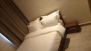 A neatly made bed with white linens and pillows, a wooden headboard, and a small wooden bench beside the bed.
