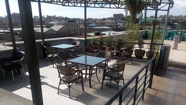A rooftop terrace with outdoor seating, including tables and chairs, surrounded by potted plants.