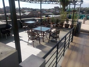 Eine Dachterrasse mit Außenbestuhlung, darunter Tische und Stühle, umgeben von Blumentöpfen.