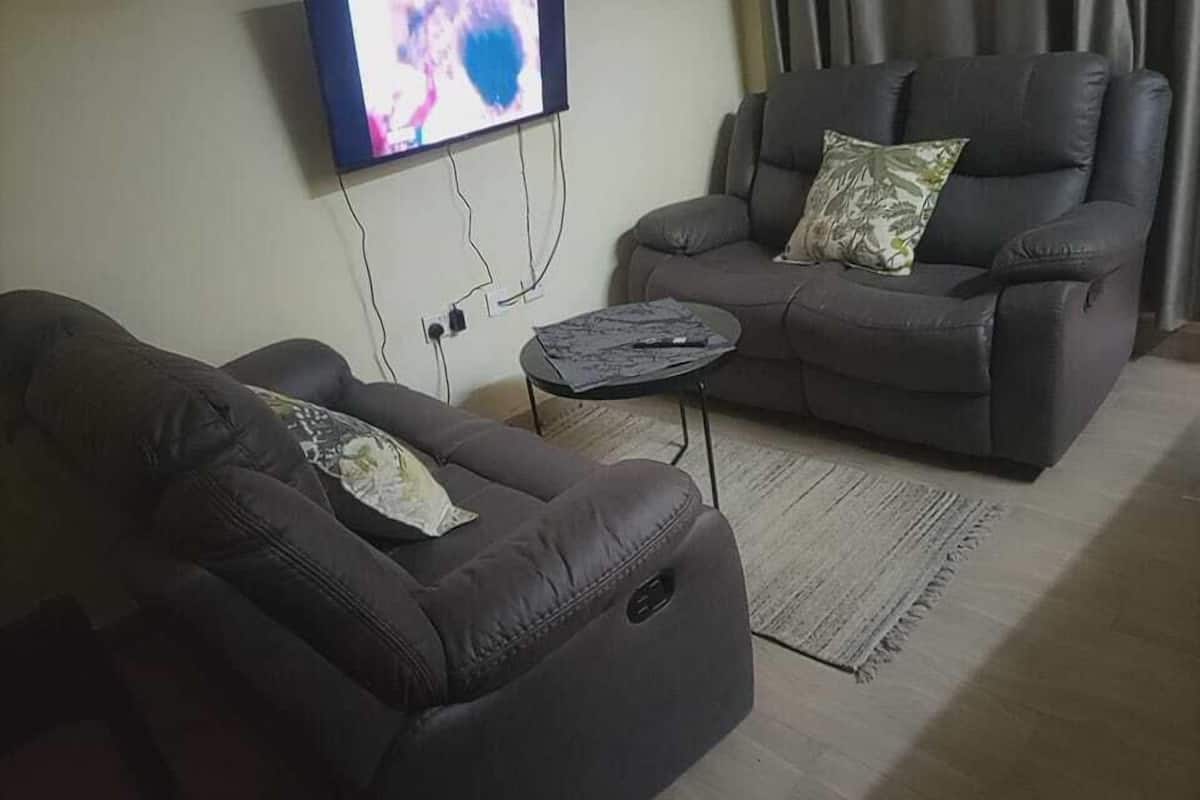 Una sala de estar con dos sofás oscuros, una mesita de centro redonda y un televisor de pantalla plana montado en la pared.