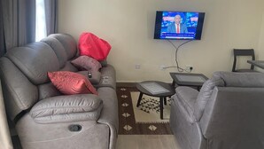 A living room with a gray sofa, a red pillow, a small table, and a television on the wall.