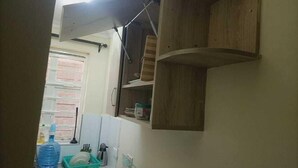 A kitchen with a built-in wooden shelf unit, a window with a view of a brick wall, and a dish rack with dishes and a water bottle.