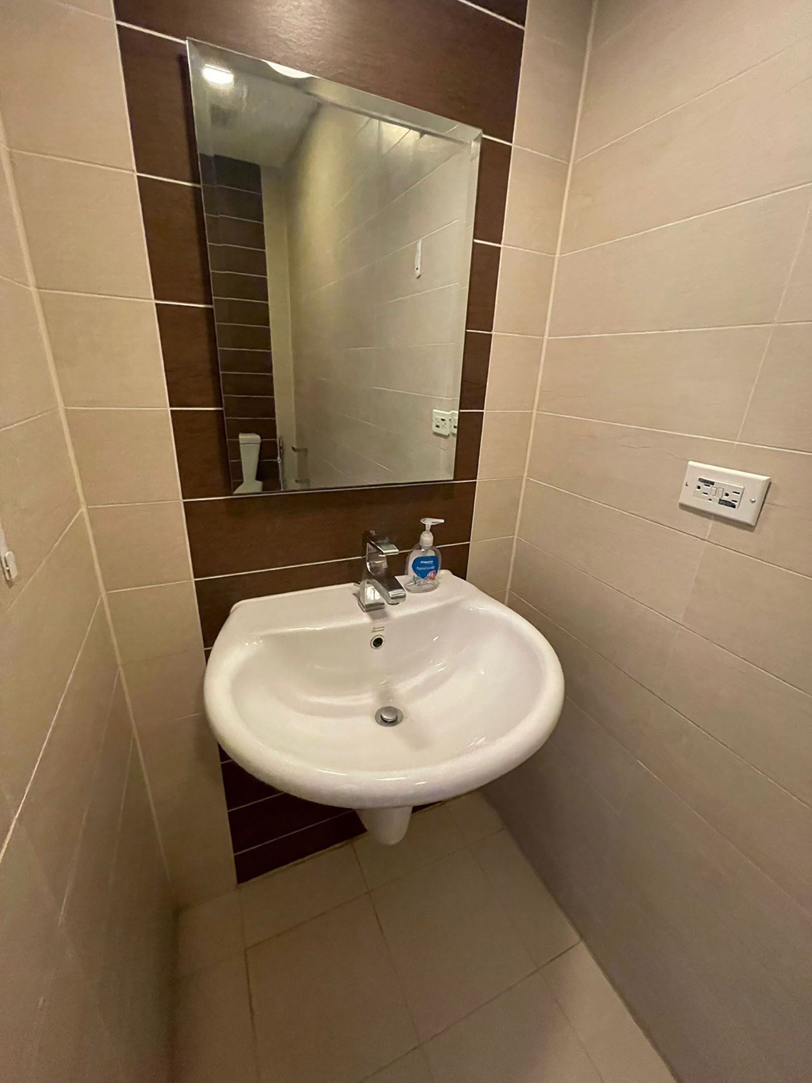Un baño con lavamanos blanco, un espejo y dispensador de jabón.