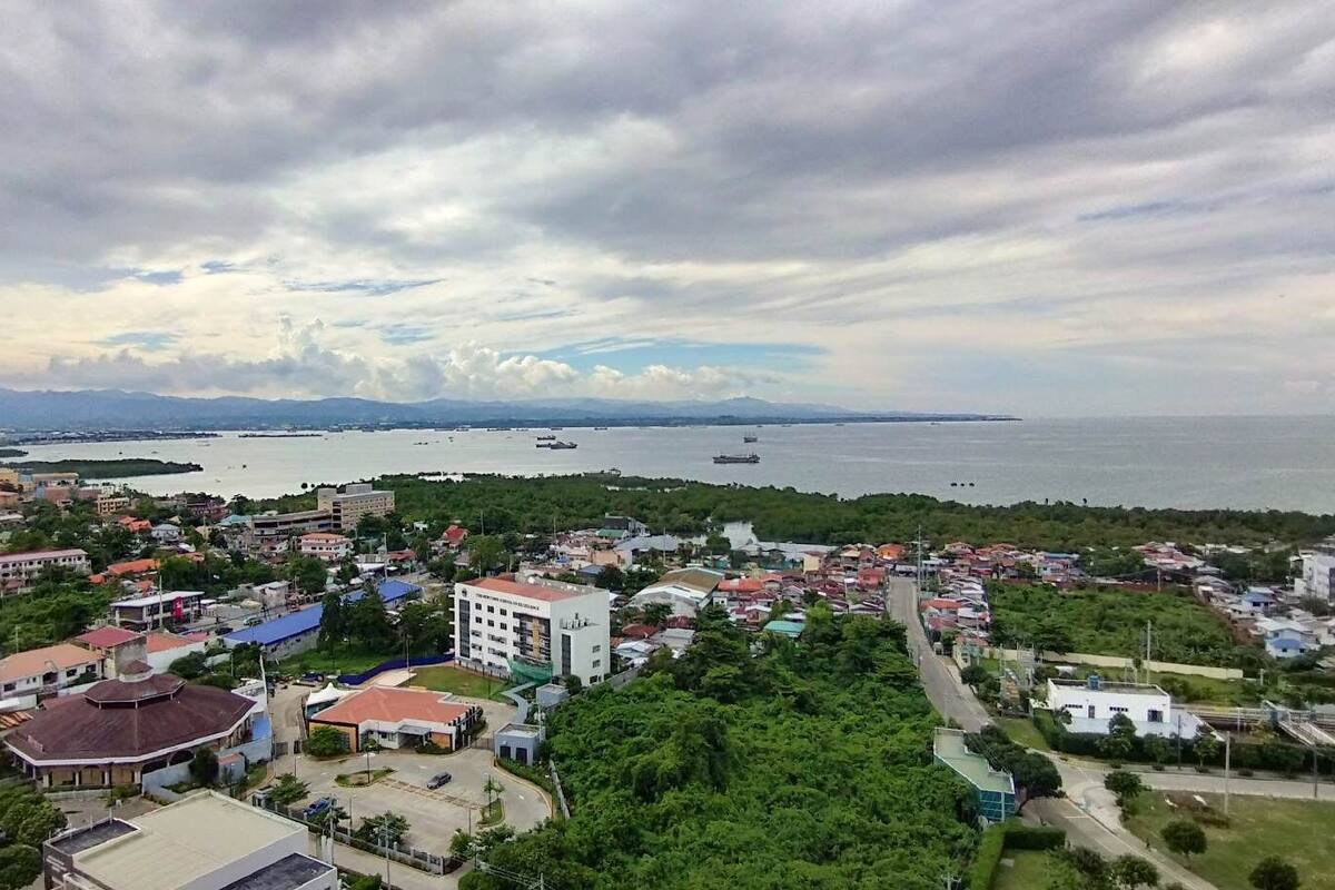 A coastal town with a mix of residential and commercial buildings, a large body of water, and a distant mountain range.
