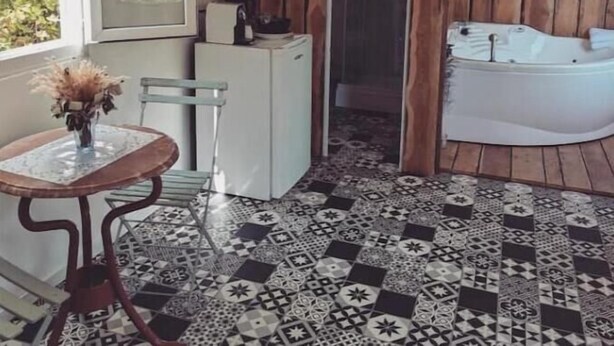 A bathroom with a bathtub, a small table with a vase, and patterned flooring. - Cabane Pour Amoureux (Daluis)