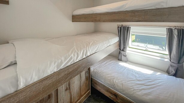 Une chambre avec un lit superposé, une fenêtre et des rideaux, une tête de lit en bois et du linge de lit blanc.