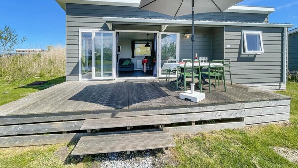 Una casa moderna con una terraza, puertas corredizas de vidrio que dan a una sala de estar y un patio con mobiliario exterior.