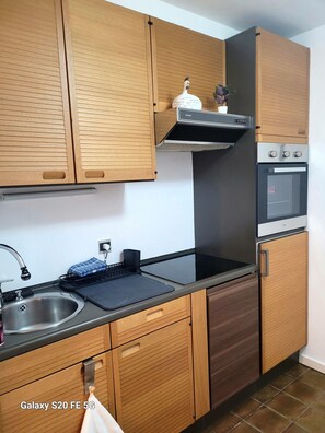 Een moderne keuken met houten kasten, een roestvrijstalen spoelbak, een zwart aanrecht, een ingebouwde oven en een afzuigkap.