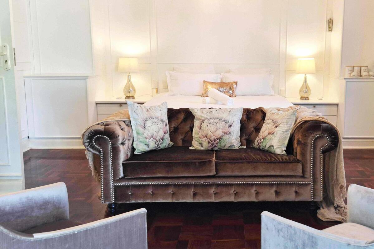A bedroom with a large, tufted brown sofa bed, two bedside lamps, and a floral-patterned throw blanket.