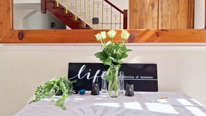 A table with a black sign reading "lipstick collection of moments," a vase with flowers, a small potted plant, and two candles with the letter "K" on them. - Akamah Estate (Cape Town)