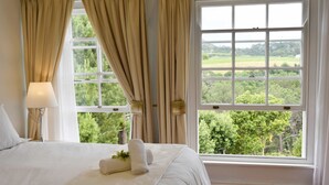 A bedroom with a large window, a bed with white linens, and a lamp on a bedside table. - Akamah Estate (Cape Town)