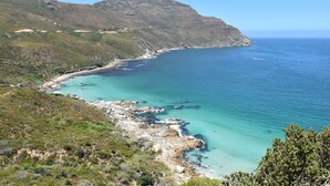 A coastal landscape with a clear view of the sea, rocky shoreline, and a mountain in the background. - Akamah Estate (Cape Town)